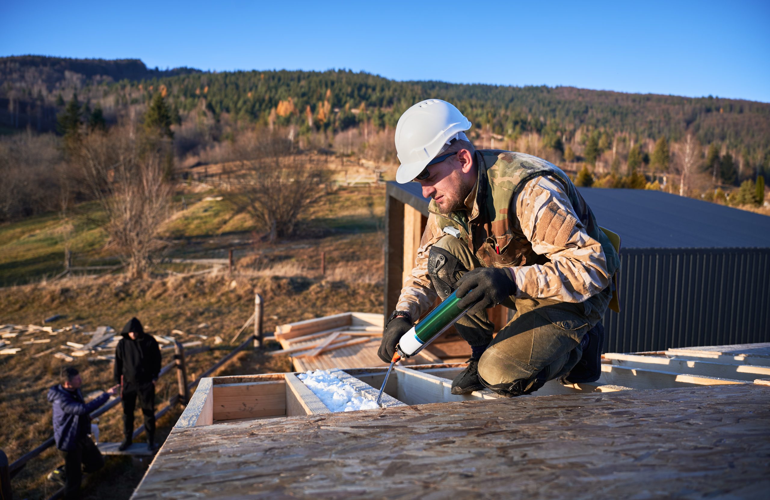 Male builder doing thermal insulation on roof of wooden frame house. Man worker spraying polyurethane foam on rooftop pros and cons of commercial roofing